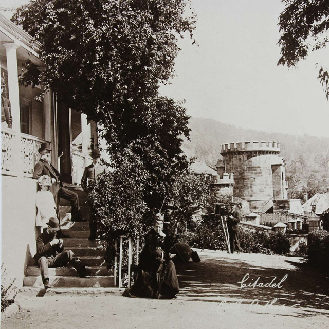 Vintage photograph of people sitting on steps of a building, with a stone tower visible in the background.