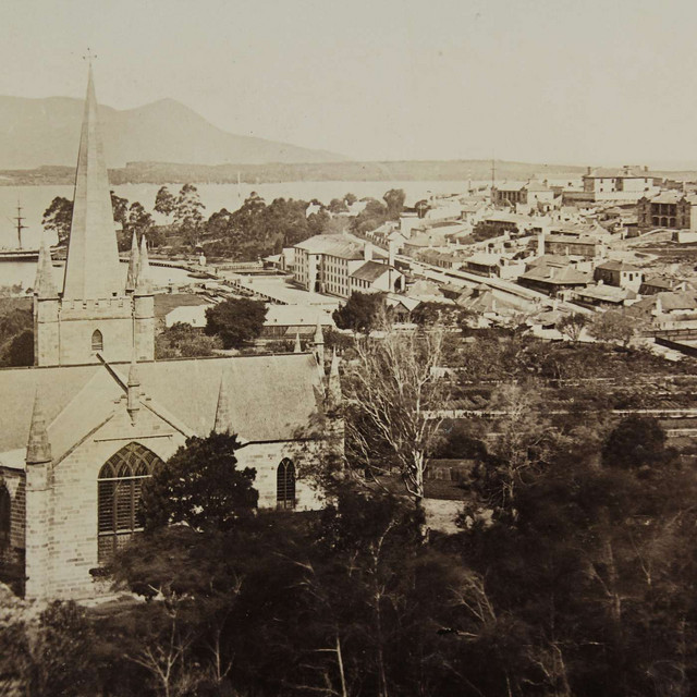 Historic aerial view of a coastal town with a prominent church spire in the foreground and mountains in the distance.